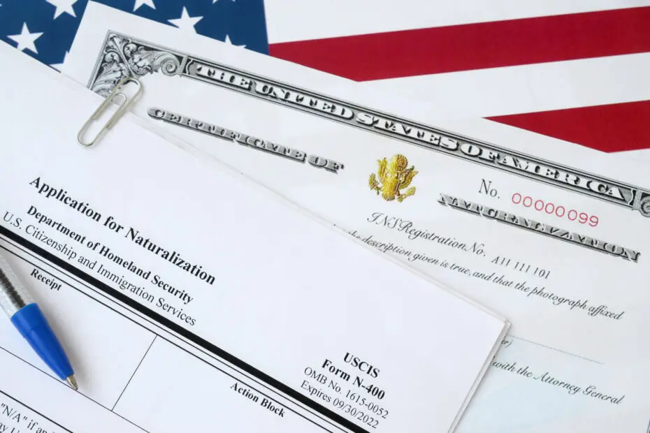 N-400 Application for Naturalization and Certificate of Naturalization documents on top of a United States flag, accompanied by a blue Department of Homeland Security pen.